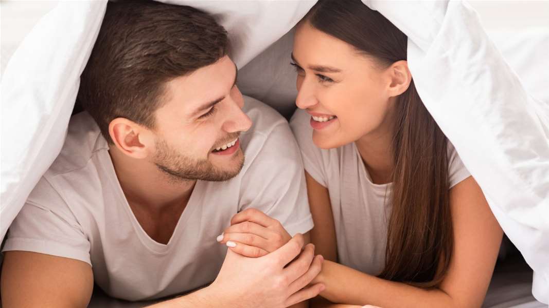 happy-couple-lying-on-bed-covered-with-blanket-in-bedroom-picture-id1201655801.jpg