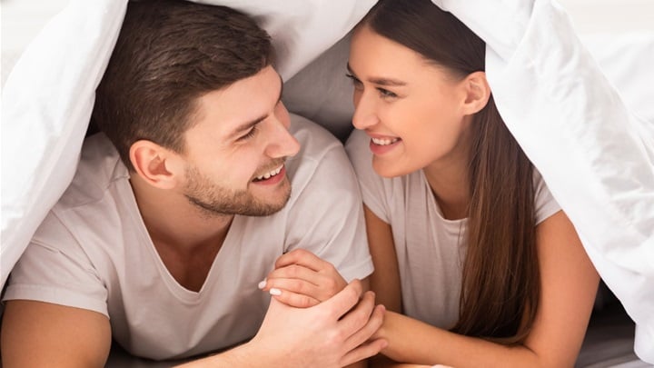 happy-couple-lying-on-bed-covered-with-blanket-in-bedroom-picture-id1201655801.jpg